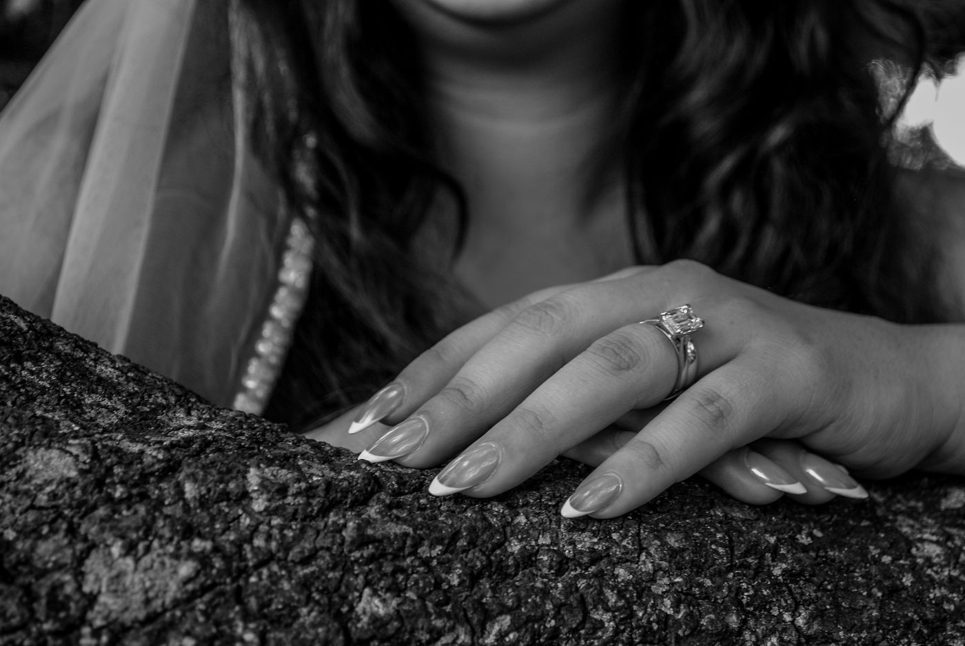 A bride's engagement ring rests on weathered bark, black and white