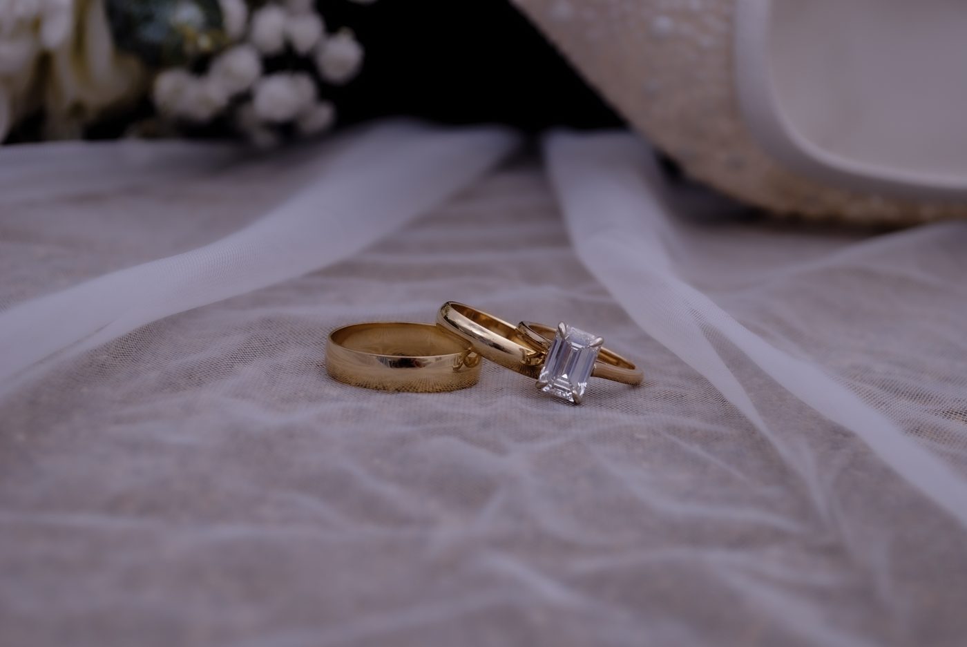 Gold wedding bands and a diamond engagement ring on white fabric