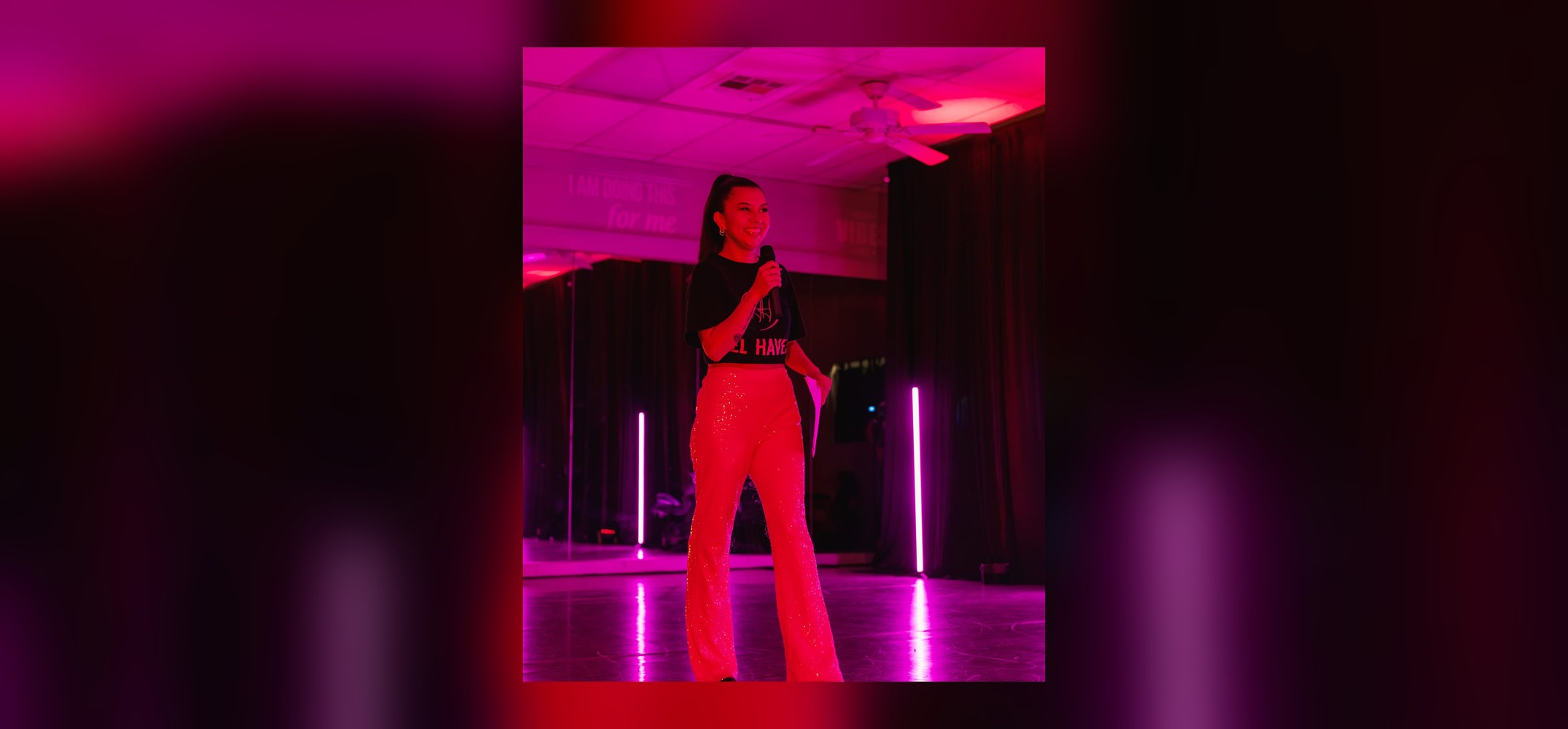 Wanda hosting an event with a microphone under vibrant pink stage lighting
