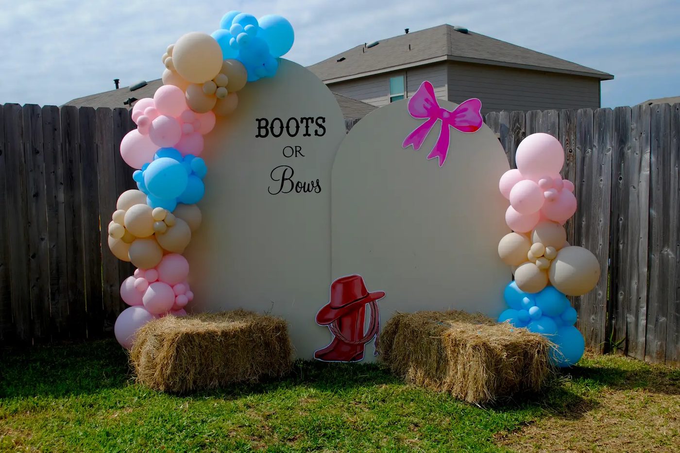 A Boots or Bows gender reveal backdrop with a pink-and-blue balloon arch and hay bales