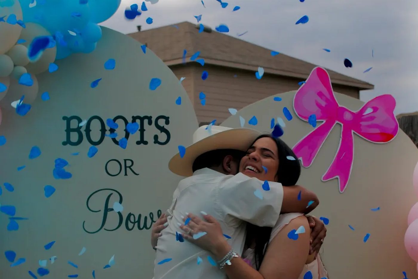 Parents-to-be embrace joyfully in a shower of blue confetti at their Boots or Bows gender reveal